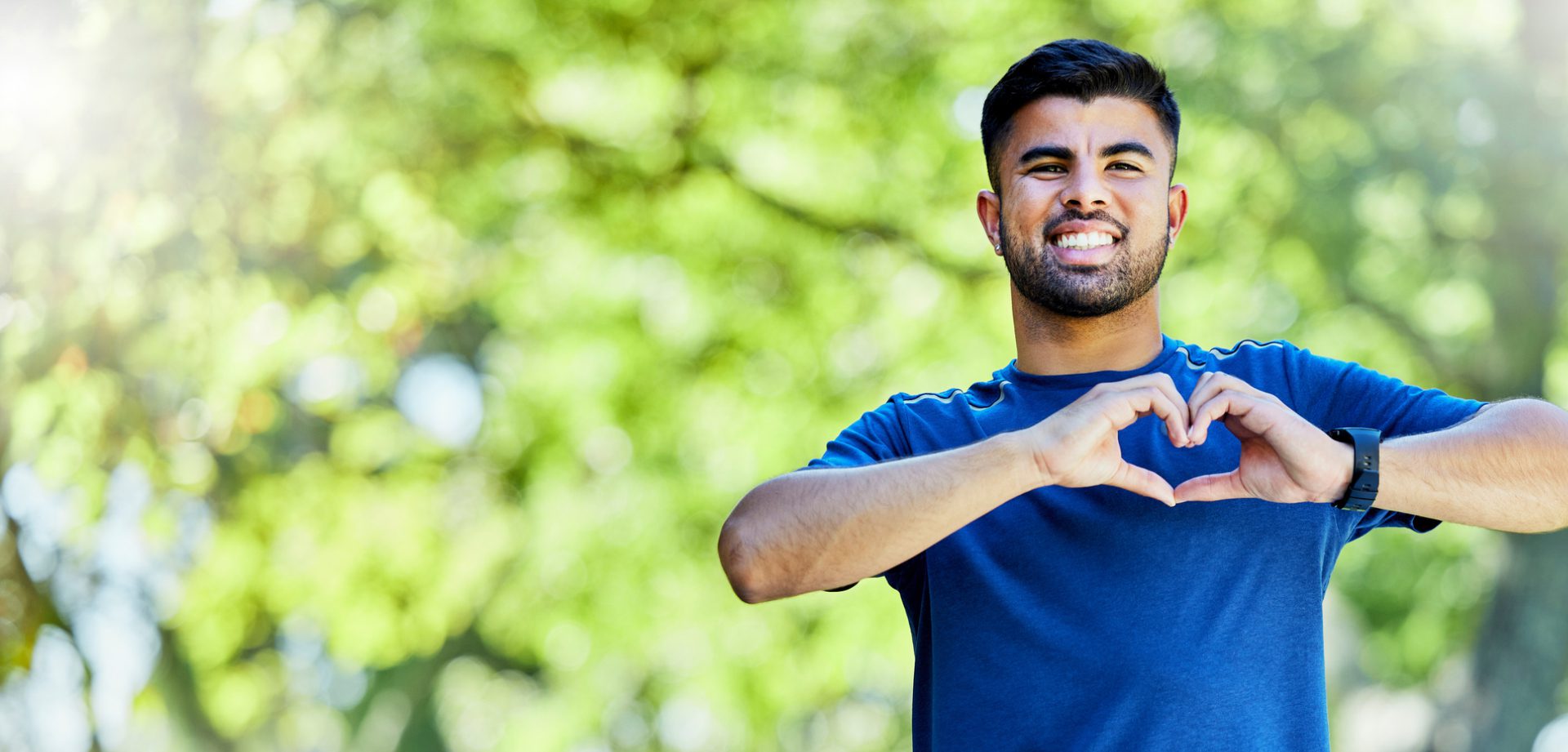 A man smiling outdoors with trees in the background.