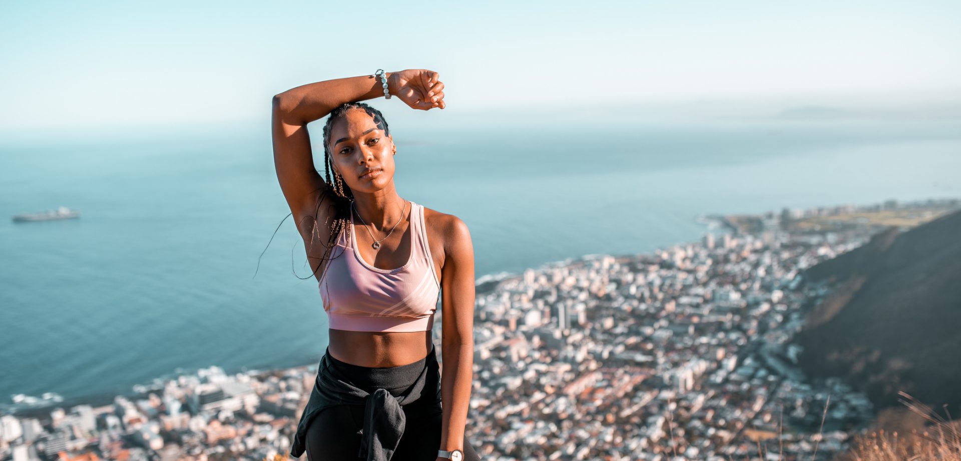Woman in workout clothes posing outdoors with a cityscape background.