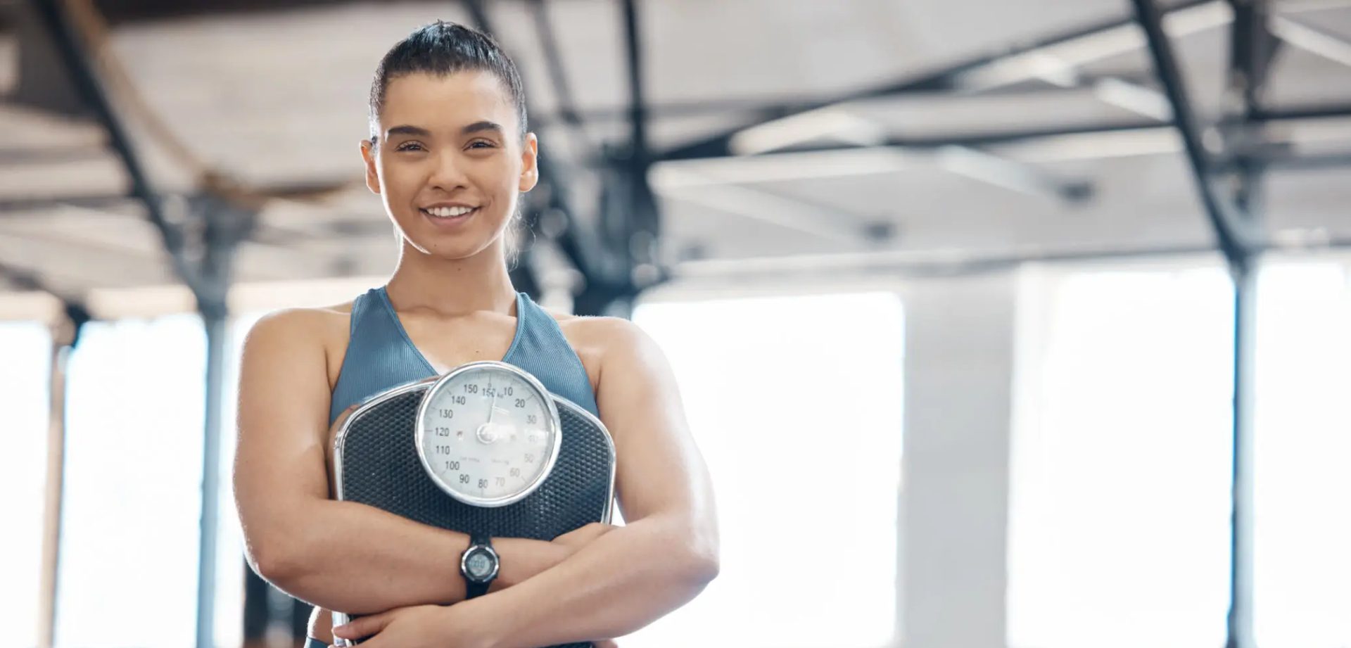 Confident woman holding a scale in a gym.