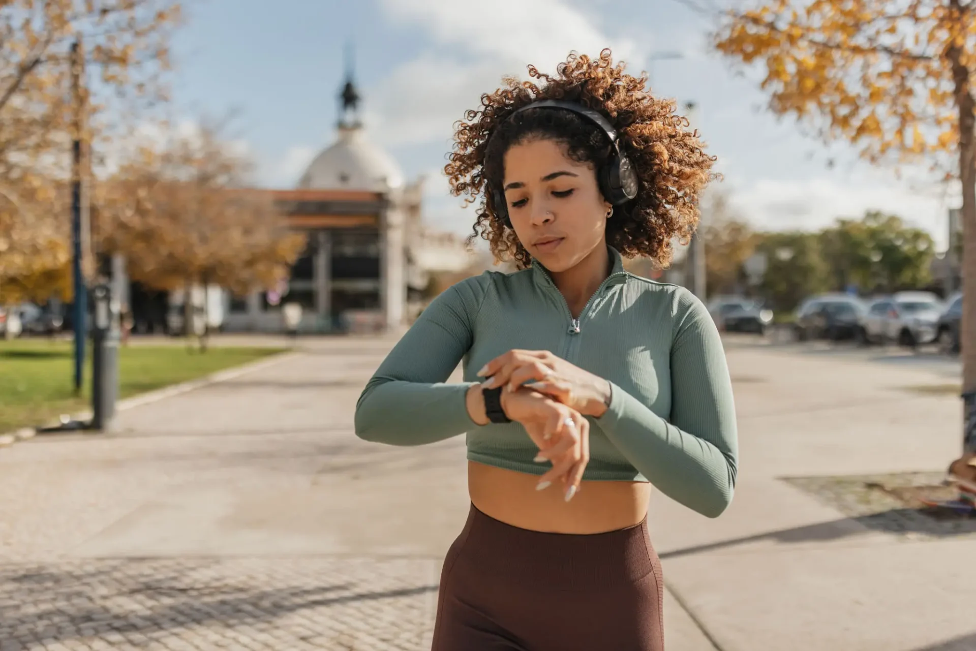 A woman checks her smartwatch outdoors in autumn.