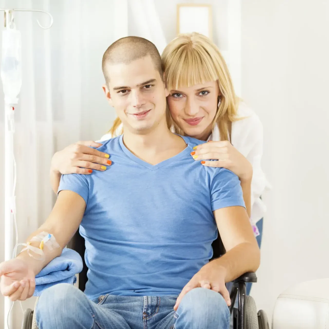 Young woman comforting a man in a wheelchair with a medical IV.