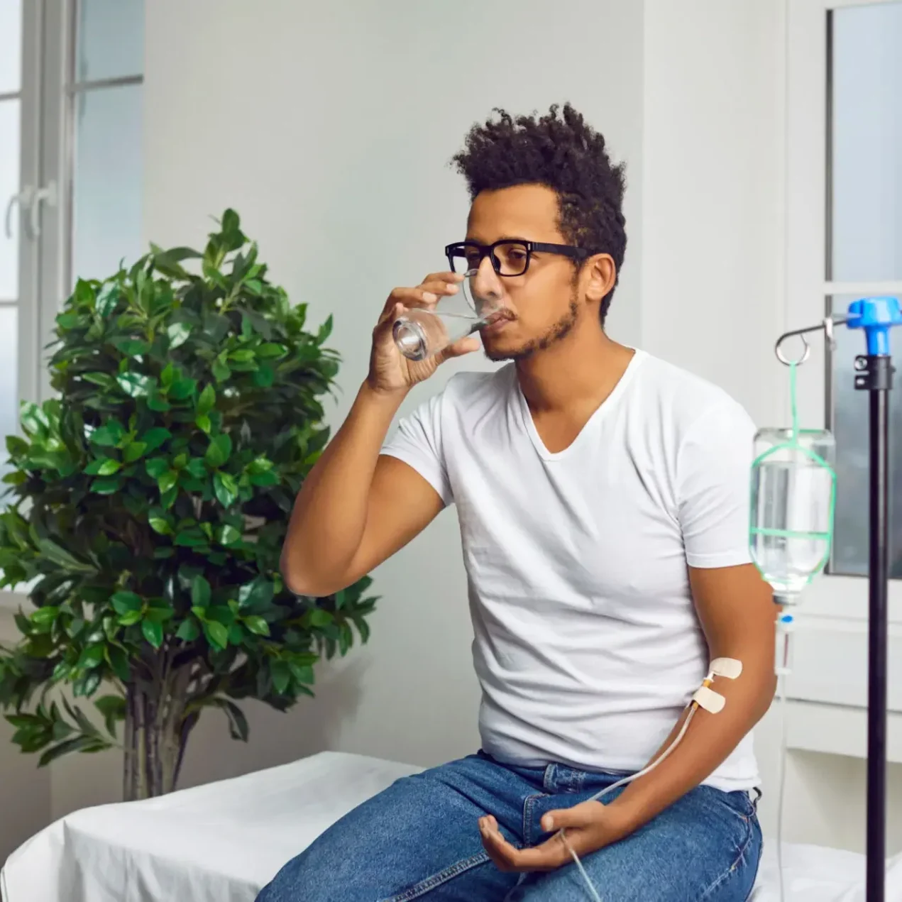 Man drinking water in a clinical setting with an IV drip.